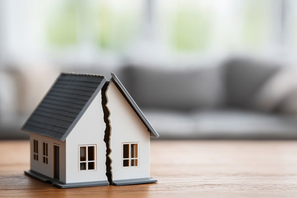 Modellhaus, das in der Mitte gerissen ist, steht auf einem Tisch, Symbol für Scheidungsimmobilien